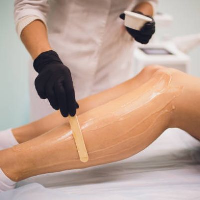 beauty, depilation, epilation, hair removal and people concept - beautiful woman with applicator applying depilatory wax to her leg